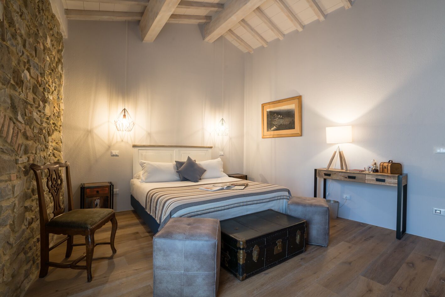 A bedroom with a bed, a chair, a desk, and a stone wall.