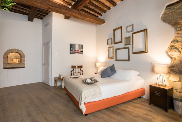 A bedroom with a bed, a nightstand, a lamp, a stone wall, and a fireplace. - Dimora delle Muse (Montalcino)