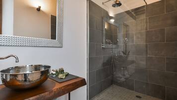 A bathroom with a large, reflective vessel sink, a wooden countertop, a mirror with a textured frame, and a glass-enclosed shower area with dark tiles.