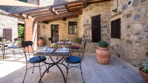 An outdoor patio with stone walls, a pergola, and a table set for dining. - Dimora delle Muse (Montalcino)