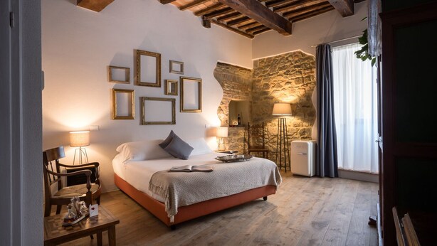 A bedroom with a bed, a chair, a table, and a stone wall. - Dimora delle Muse (Montalcino)