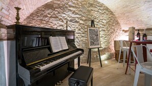 A piano with sheet music, an easel with a drawing, and a wine bottle in a stone-walled room. - Dimora delle Muse (Montalcino)