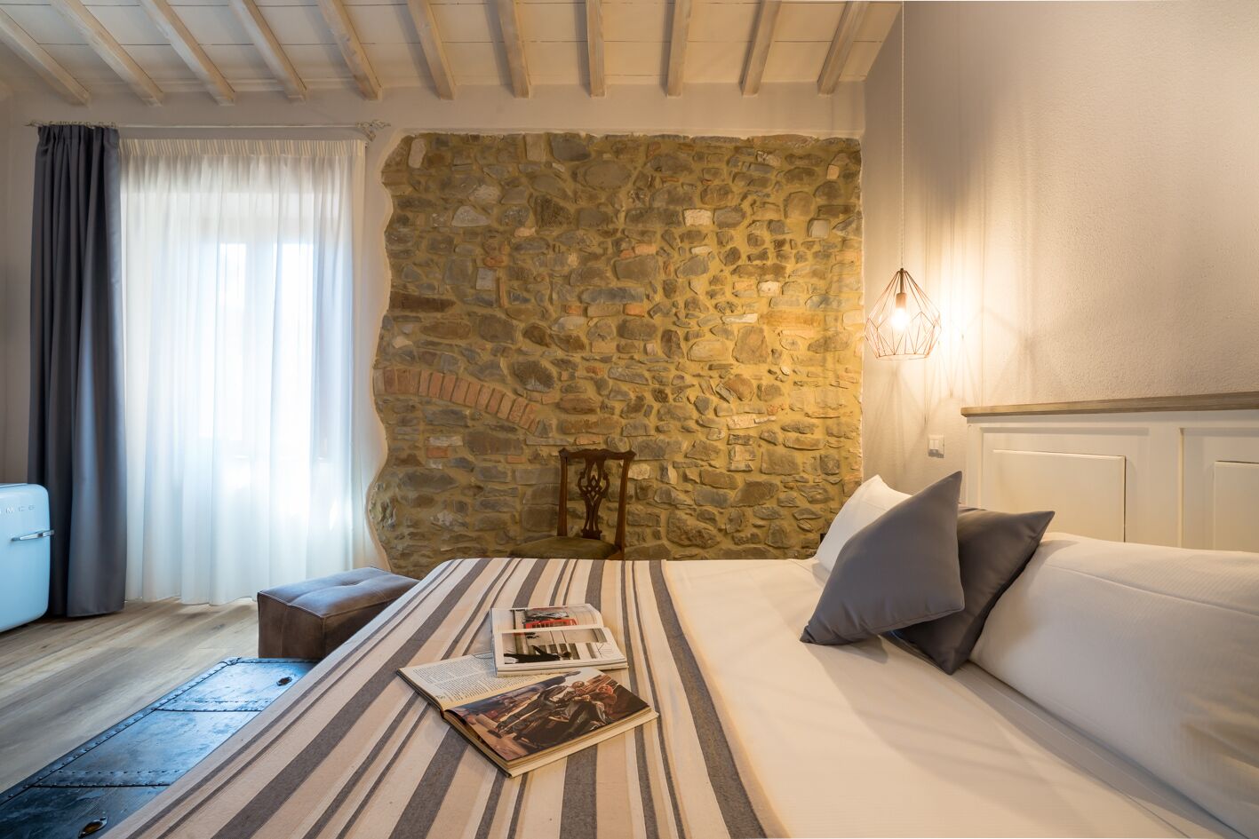 A bedroom with a stone wall, a bed with pillows, a bedside table, and a lamp.