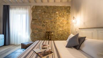 A bedroom with a stone wall, a bed with pillows, a bedside table, and a lamp.