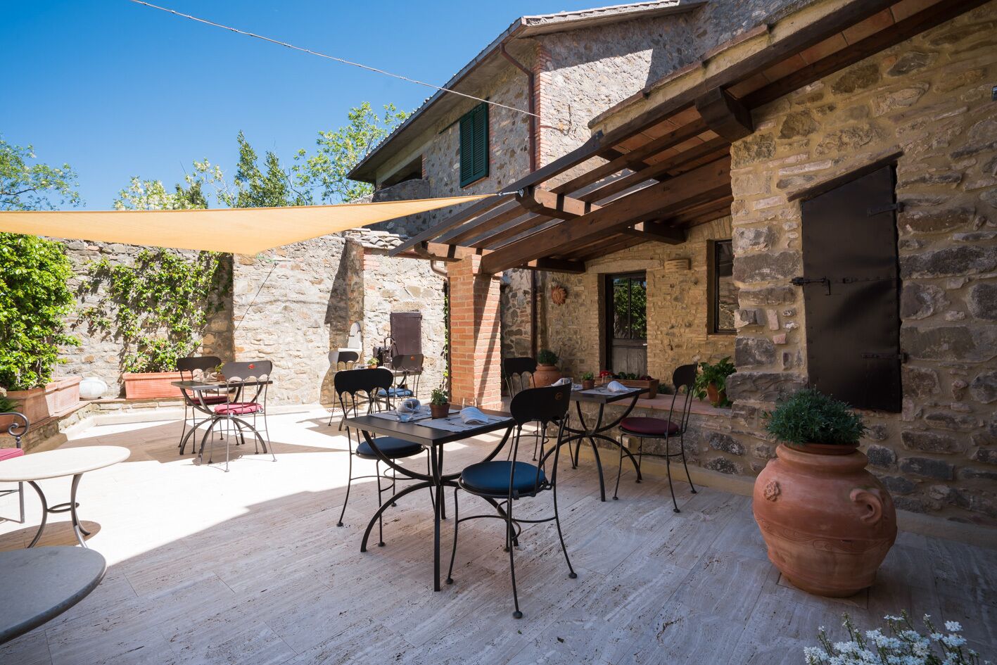 Eine Terrasse im Freien mit Steinmauern, Holzbalken sowie Tischen und Stühlen.