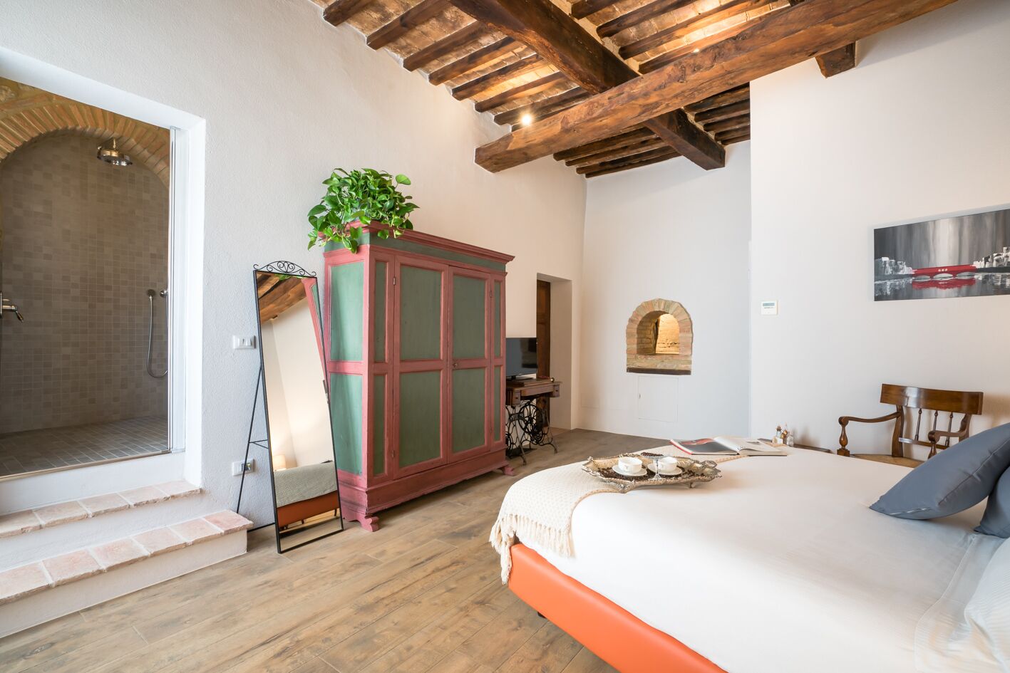A bedroom with a wooden ceiling, a large bed, a wardrobe, a shower, and a small table with a tray.