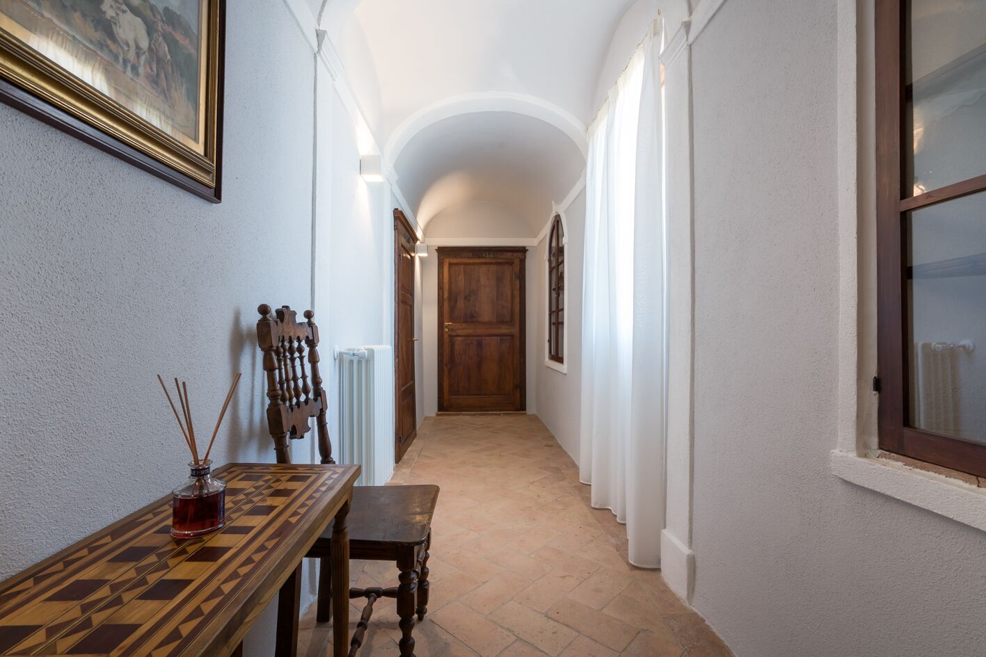 A narrow hallway with a wooden table and chairs, a radiator, and a door at the end.