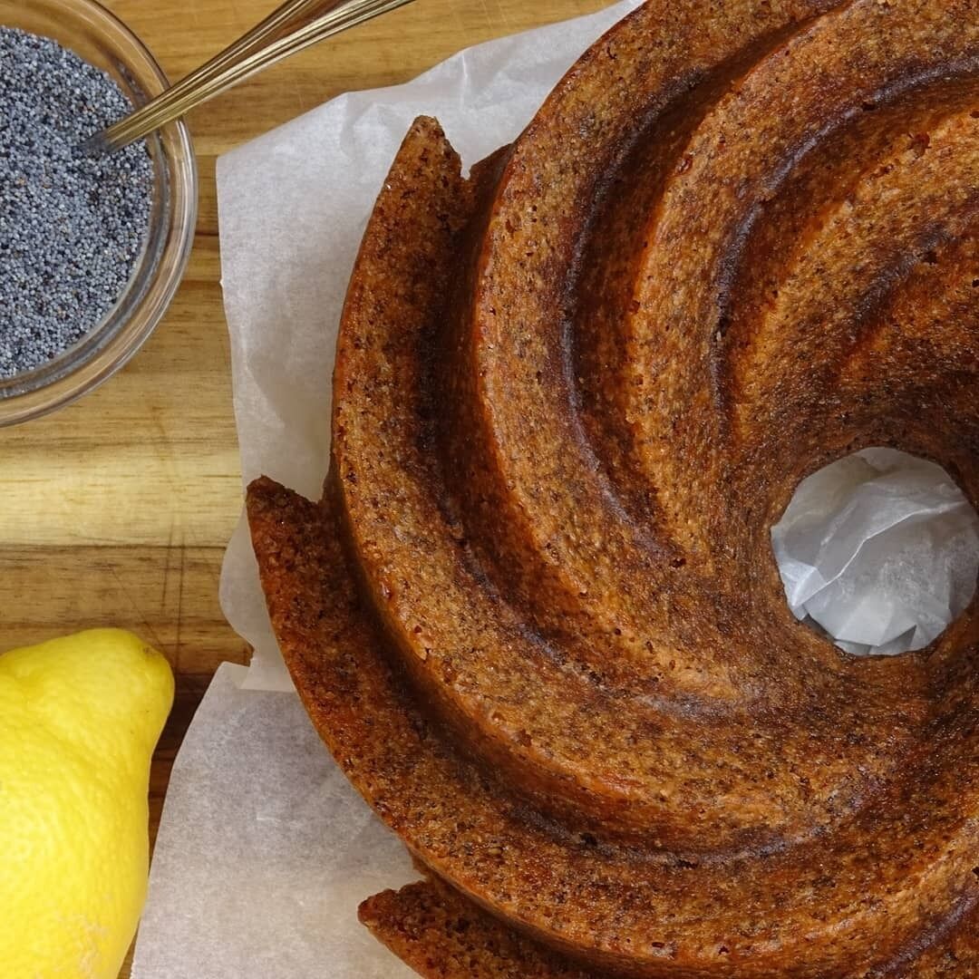 Ein Kuchen mit Spiralmuster, auf einer Holztischplatte zusammen mit einem Löffel und einer Schüssel mit blauem Pulver.