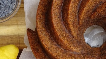 Ein Kuchen mit Spiralmuster, auf einer Holztischplatte zusammen mit einem Löffel und einer Schüssel mit blauem Pulver.