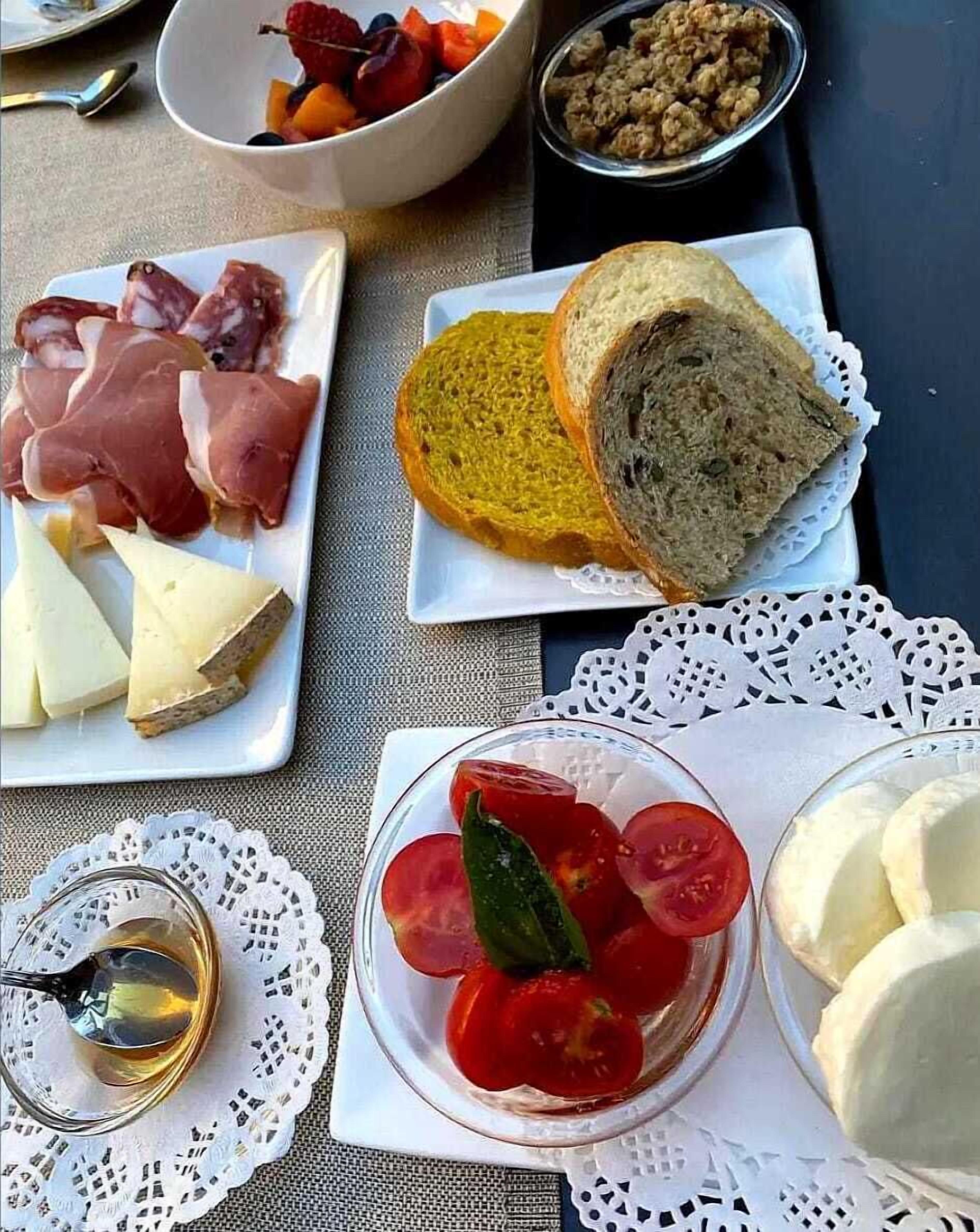 Uma mesa com diversos alimentos, incluindo embutidos, queijo, pão, tomates e uma taça de vinho.