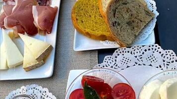Uma mesa com diversos alimentos, incluindo embutidos, queijo, pão, tomates e uma taça de vinho.