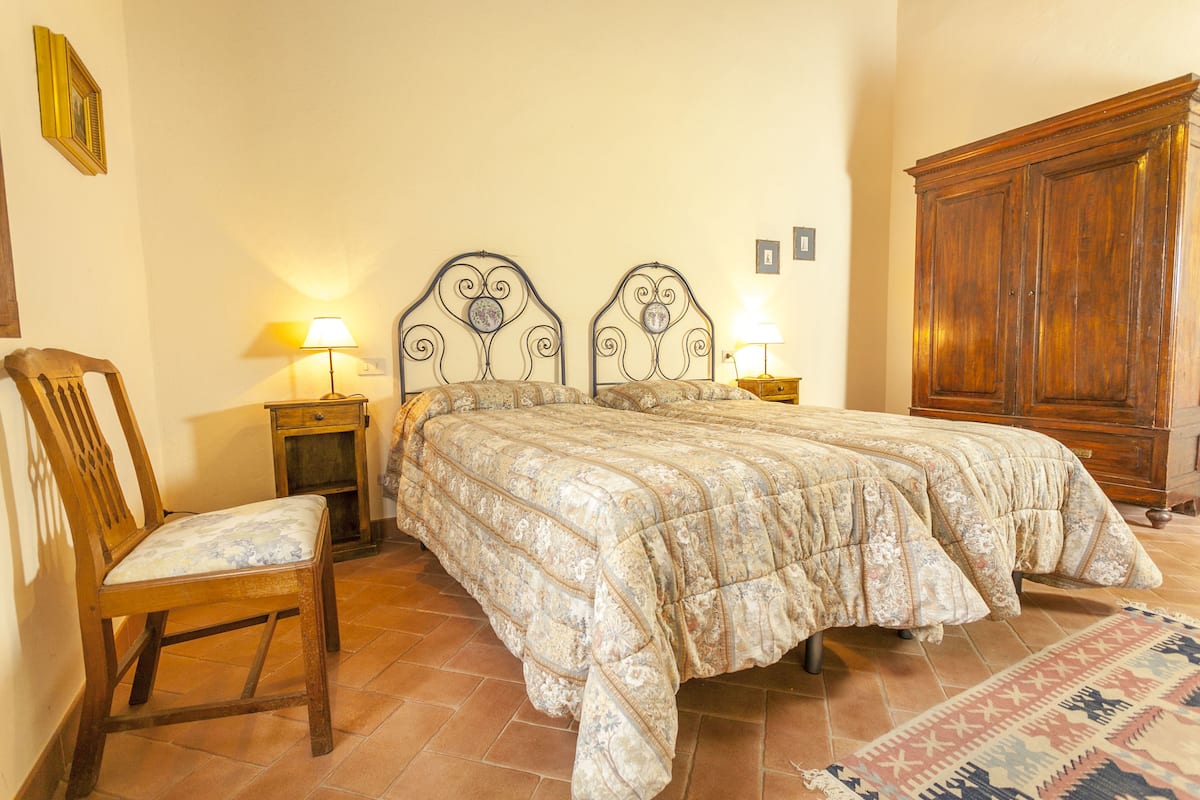 Une chambre avec deux lits, une chaise en bois, une table de chevet avec une lampe et une armoire.