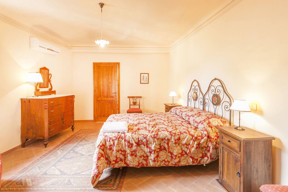 Une chambre à coucher avec un lit, une commode en bois, une table de chevet et une porte.