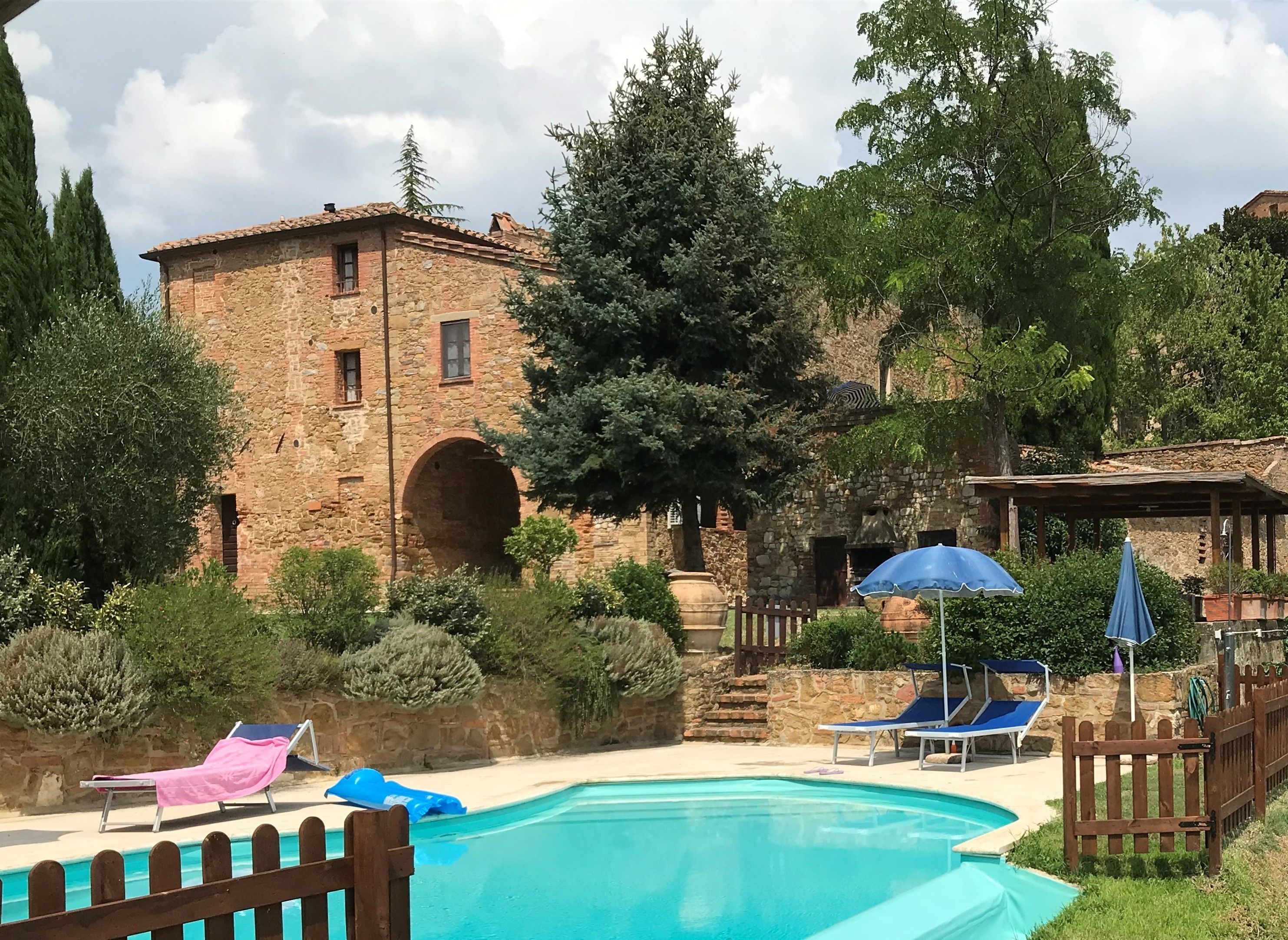 A stone building with a pool, surrounded by trees and a wooden fence.