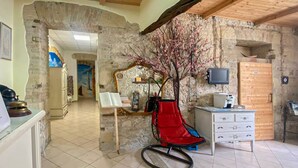 A room with a stone wall, a red chair, a white dresser, and a television. - Le Tre Stelle (Cagliari)
