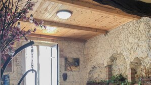 A room with a stone wall, a wooden ceiling, a red and white chair, a sofa with cushions, and a small table with a plant. - Le Tre Stelle (Cagliari)