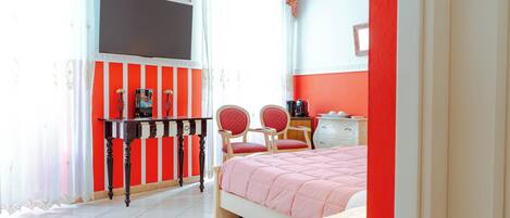 A bedroom with a bed, two chairs, a desk, a TV, and a dresser.