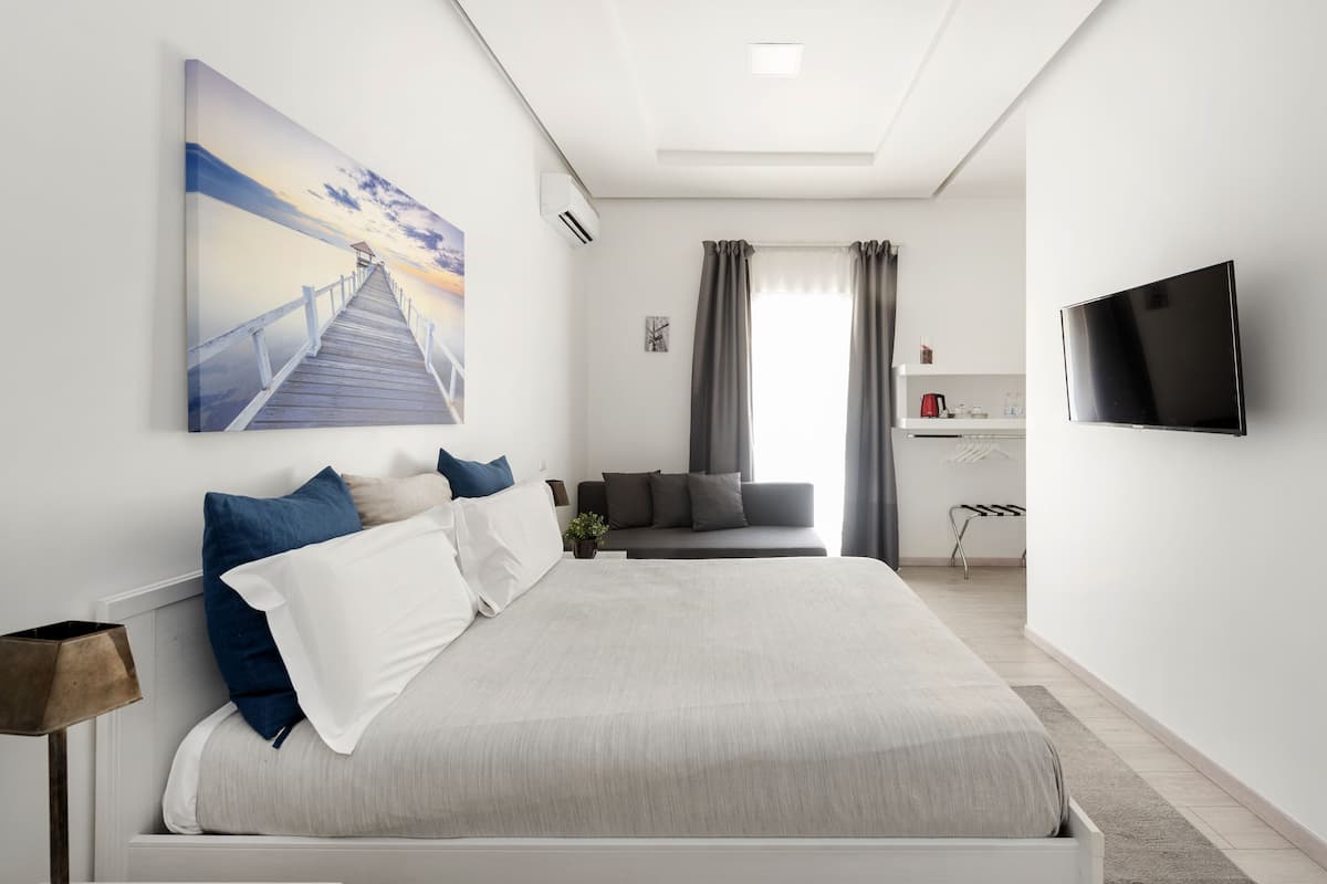 A modern hotel room with a large bed, a flat-screen TV, a desk area, and a view of a sunset over a pier.