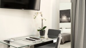 A modern hotel room with a glass desk, a potted orchid, a flat-screen TV, and a bed with a view of a forest.
