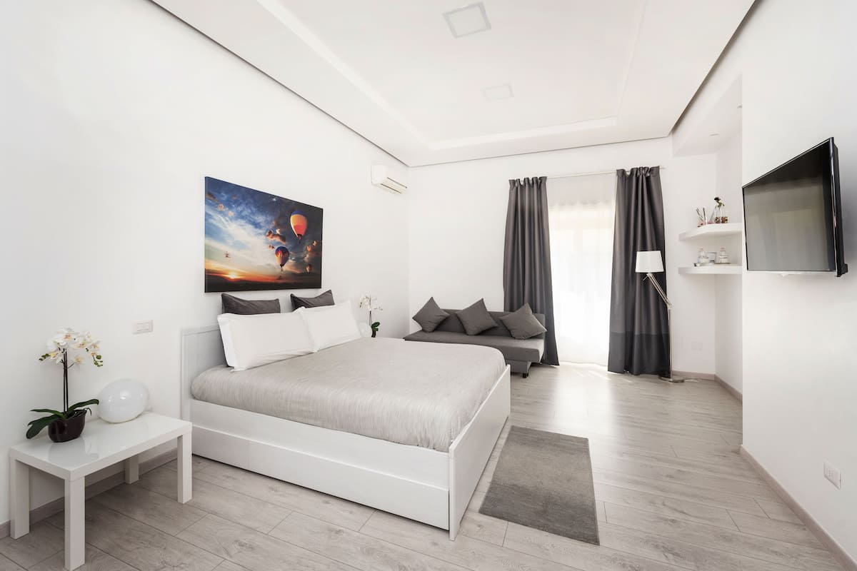 A modern bedroom with a large bed, a bedside table, a TV, and a painting of hot air balloons.
