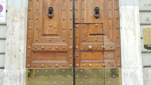 A large wooden double door with metal studs and a brass lower section, set in a building with a numbered plaque.