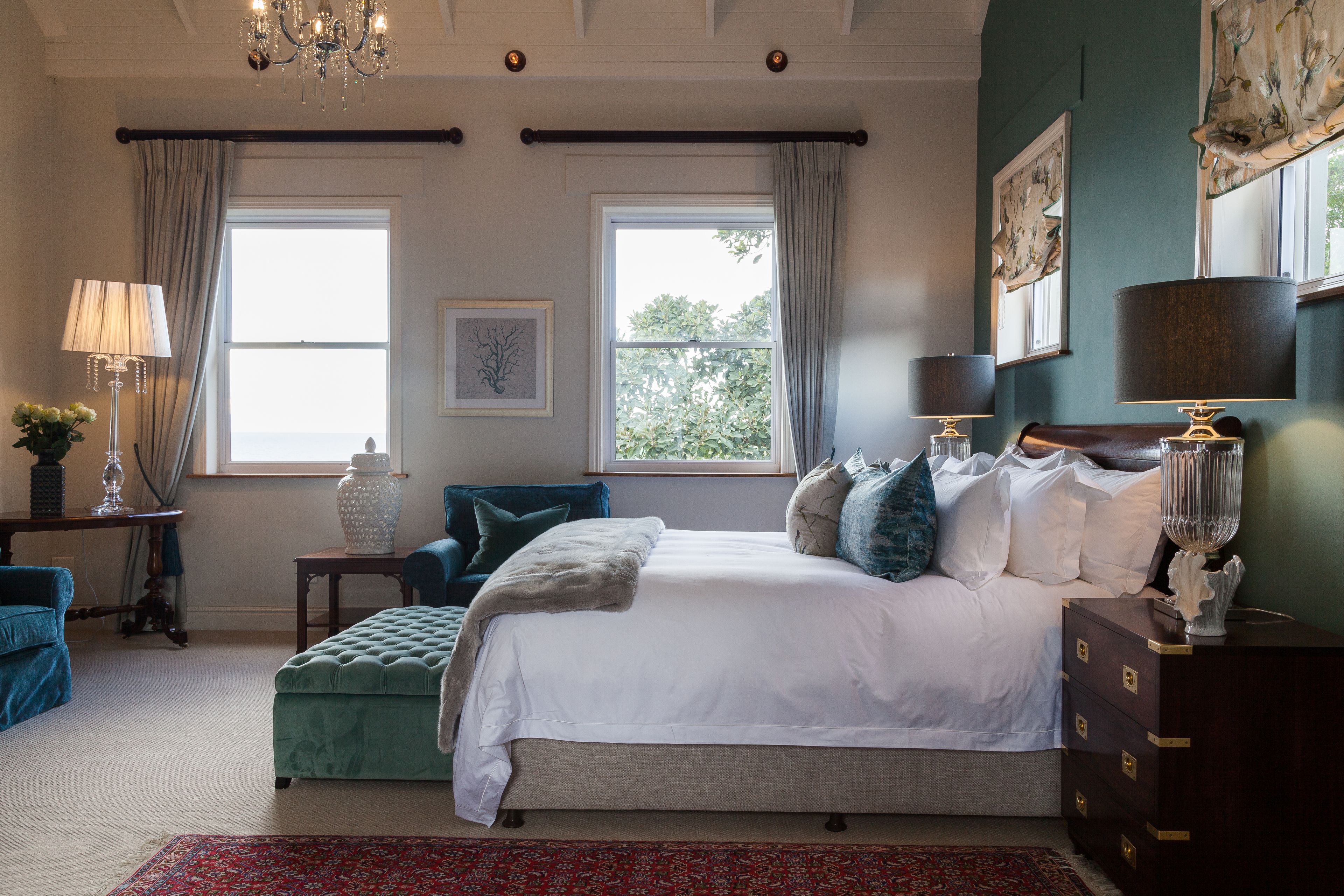 Une chambre à coucher avec un grand lit, deux fenêtres, un lustre et une commode.