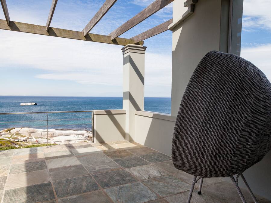 A balcony with a view of the sea, a wicker chair, and stone tiles.