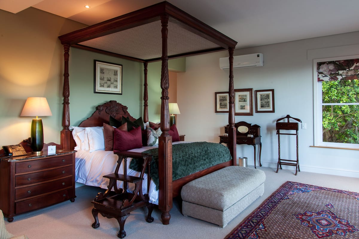 Un lit à baldaquin avec une couvre-lit verte, une table de chevet en bois avec une lampe, une petite table avec une chaise et un tapis à motifs.