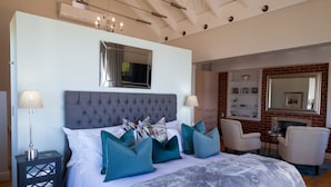 Un dormitorio con una cama grande, dos mesitas de noche, un espejo y un área de descanso con sillas y una pequeña mesa.