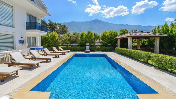 Una piscina con sillas de descanso, un área de estar cubierta y vistas a la montaña.