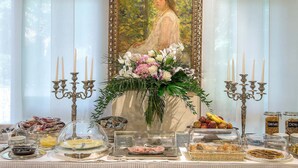 Montaje de desayuno tipo buffet con una variedad de alimentos, incluyendo frutas, pasteles y platos para el desayuno, sobre una mesa con un fondo decorativo.