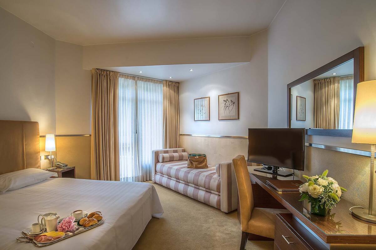 A hotel room with a bed, a desk, a chair, a TV, and a window with curtains.