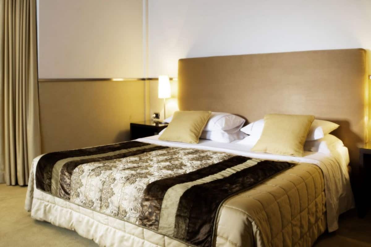 A hotel room with a large bed, a nightstand with a lamp, and a view of the city through the window.