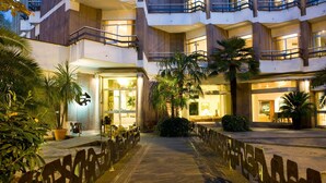 Entrada de hotel con un corredor techado, palmeras y una fachada bien iluminada.