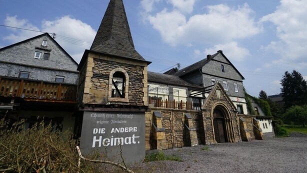A historic building with a prominent stone tower and a sign reading "Die Andere Heimat." - Hotel Restaurant Gemünden (Gemuenden)