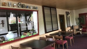 A restaurant interior with wooden tables and chairs, a large window with decorative items, and a traditional sliding door. - Hotel Restaurant Gemünden (Gemuenden)