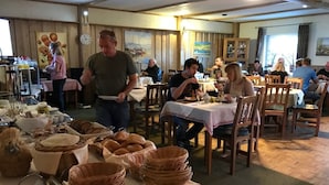 A dining area with tables set for meals, baskets of bread, and a person serving food. - Hotel Restaurant Gemünden (Gemuenden)