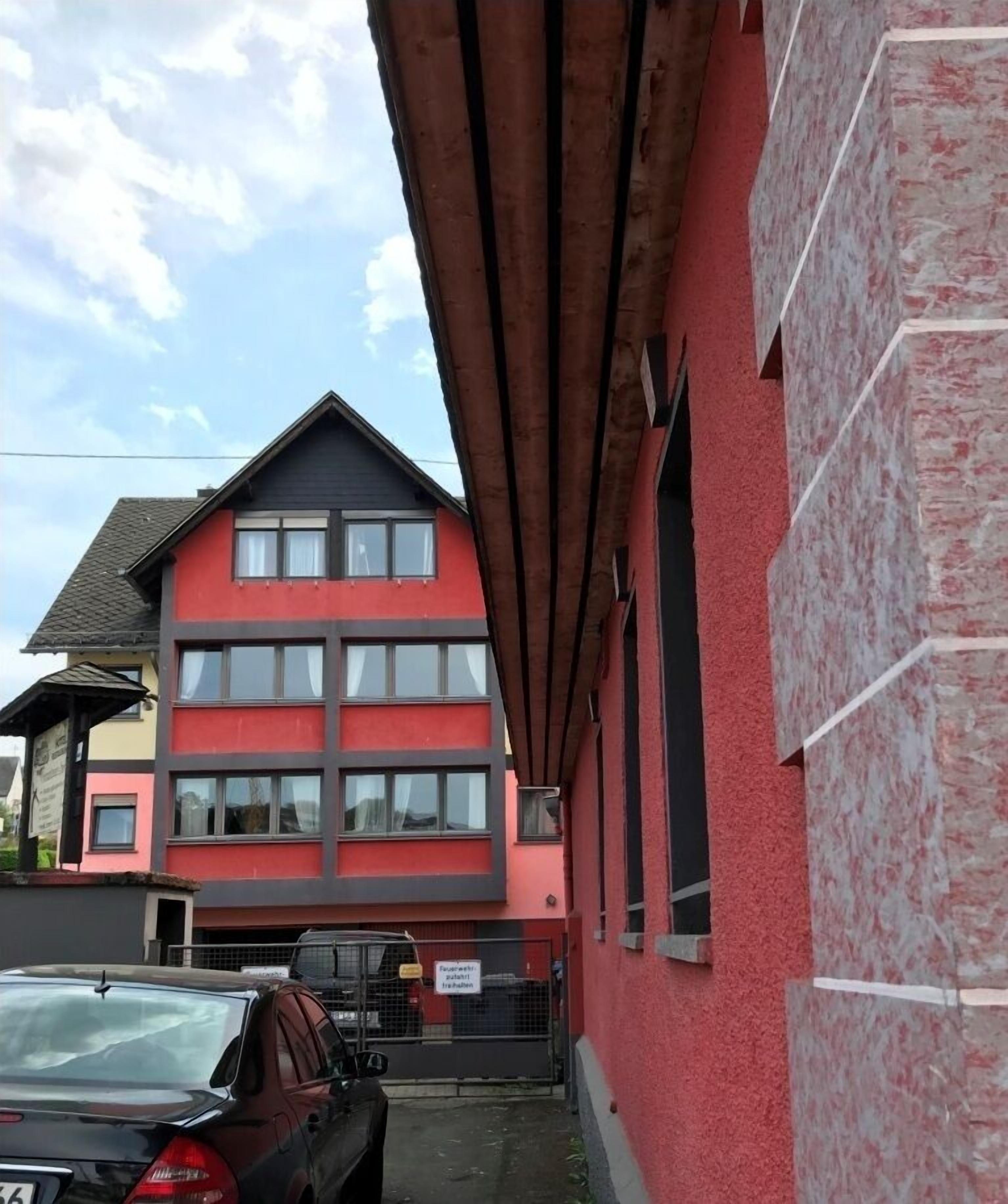 Un immeuble à plusieurs étages, doté d’une façade rouge et grise, de grandes fenêtres et d’une entrée de garage bien visible.