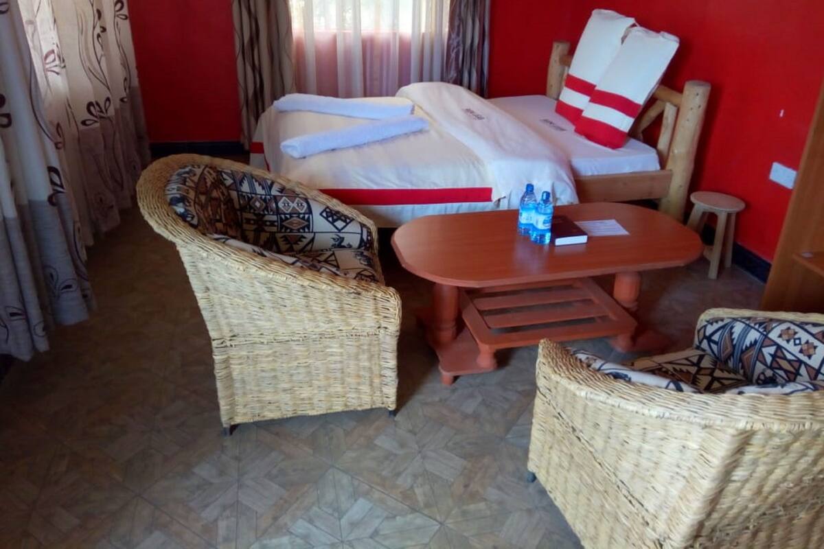 A hotel room with a bed, two wicker chairs, a small wooden table, and a window with curtains.