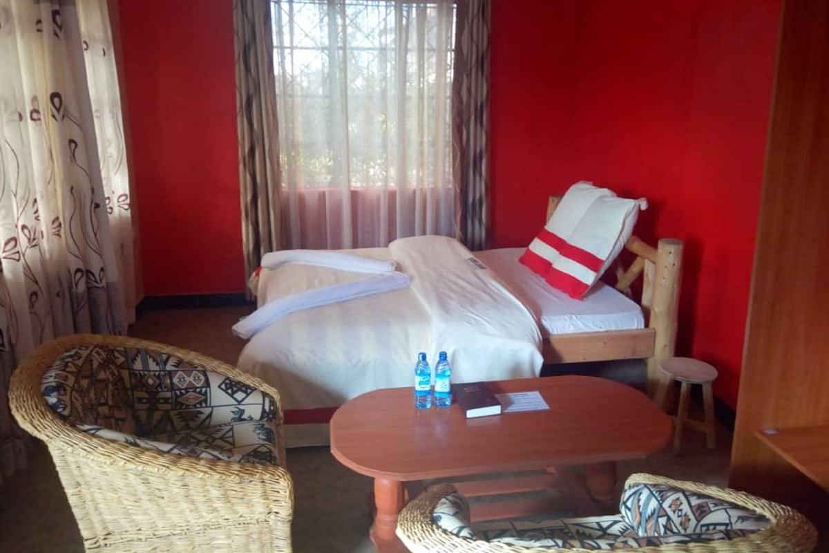 A hotel room with a bed, two wicker chairs, a wooden table, and a window with curtains.