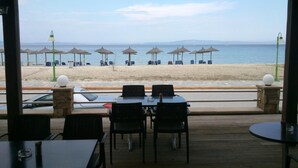 An outdoor seating area with tables and chairs facing a beach. - Meltemi Rooms (Sithonia)