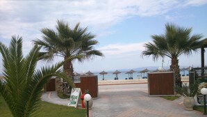 A pathway leading to a beach area with palm trees and beach umbrellas. - Meltemi Rooms (Sithonia)