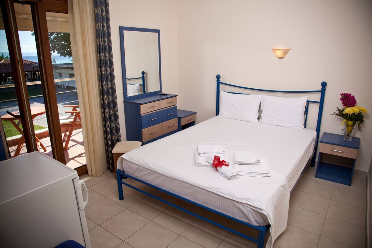 Habitación de hotel con cama, cómoda, mesita de noche, espejo y ventana con vistas al exterior.