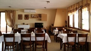 A dining area with multiple tables and chairs, a television, and decorative items on the walls. - Meltemi Rooms (Sithonia)