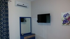 A bedroom with a blue dresser, a small stool, an air conditioning unit, and a wall-mounted TV. - Meltemi Rooms (Sithonia)