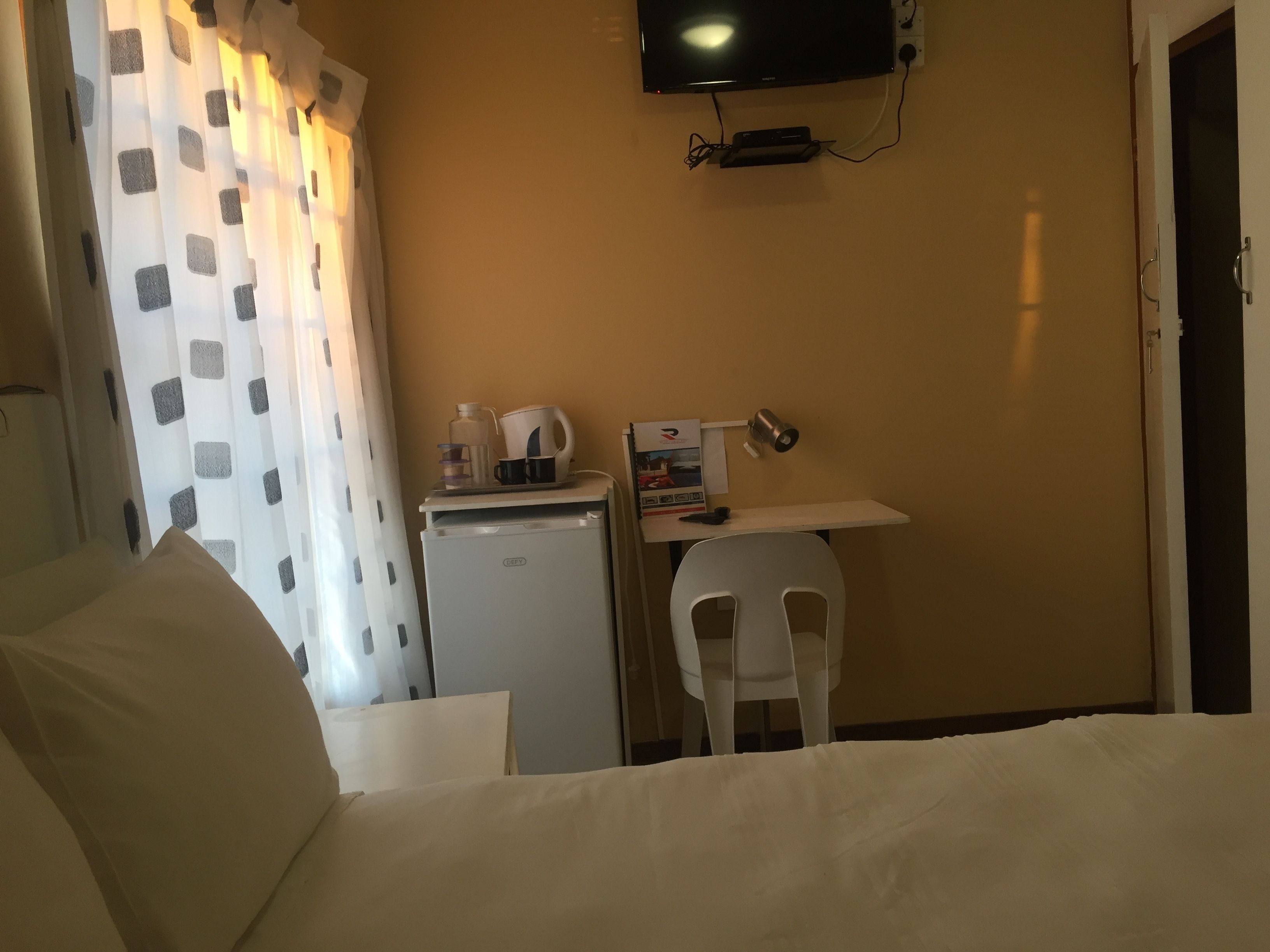 A hotel room with a bed, a desk with a computer, a refrigerator, a TV mounted on the wall, and a chair.