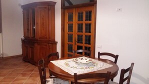 A dining area with a round wooden table, four chairs, a floral tablecloth, and a wooden cabinet. - Agriturismo San Filippo (Acquapendente)