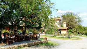 A rustic outdoor seating area with wooden furniture and potted plants, surrounded by trees and a building with a tiled roof. - Agriturismo San Filippo (Acquapendente)