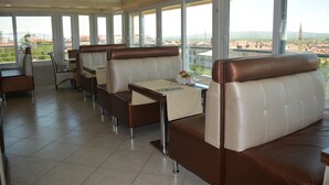 Un restaurante con asientos tipo cabina de respaldo alto, piso de baldosas y grandes ventanales con vistas a la ciudad.