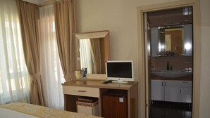Habitación de hotel con cama, escritorio con computadora, espejo, lavamanos y armario.